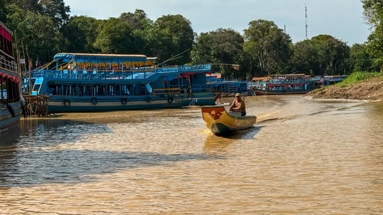 A fisherman in a traditional boat heading out to work passing tourist boats.